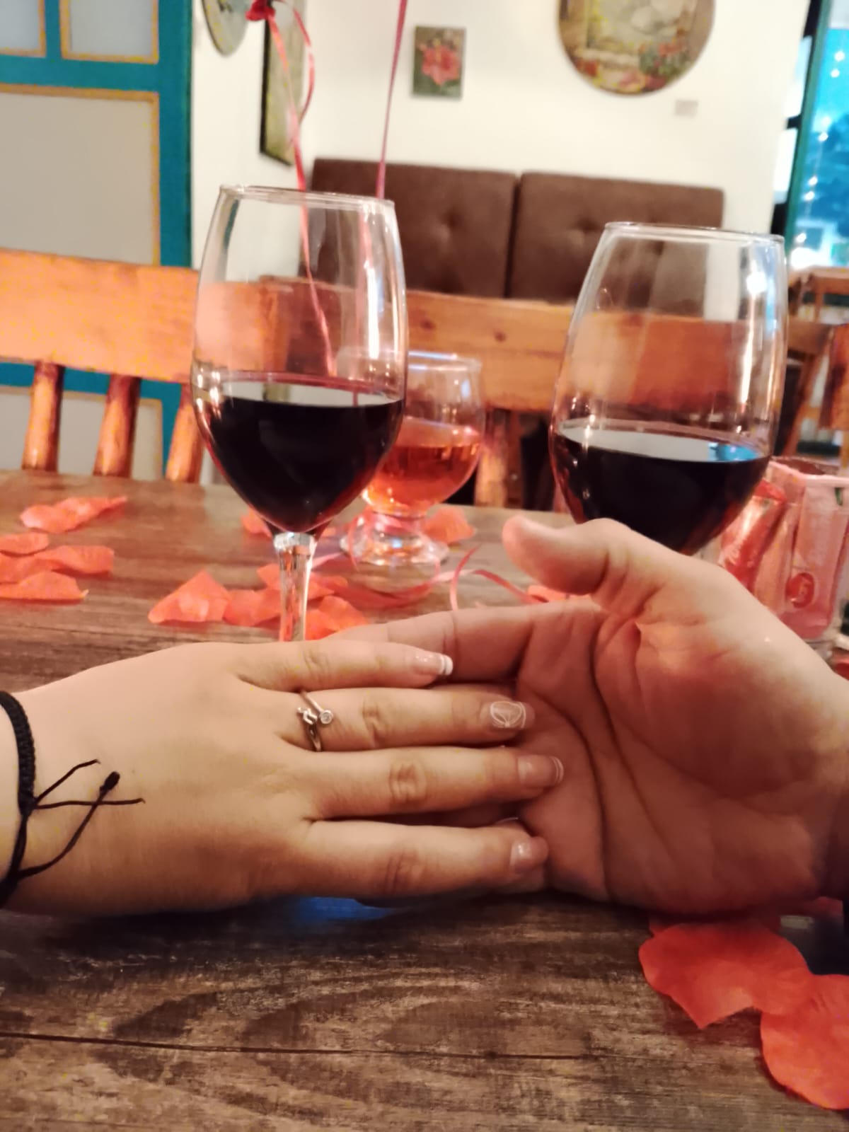 Cena romántica con dos copas de vino y pétalos de rosa sobre la mesa de madera